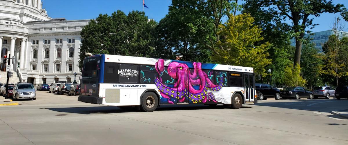 Bus driving in front of state capital with full ad graphic of a pink octopus