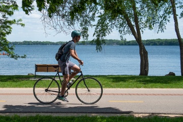 Person biking on a street next to a lake.