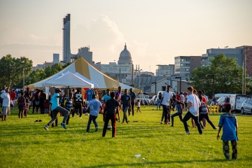 Group of people playing soccer. There are large event tents in the background.